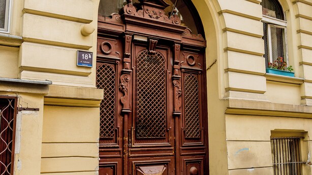 A large, ornate wooden door with intricate carvings and a number plate indicating the address.
