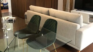 Una sala de estar moderna con un sofá, una mesa de vidrio con sillas, un televisor y elementos decorativos.