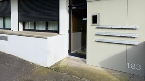 Entrada de un edificio con una persiana cerrada, un letrero que dice "BLOCOG 183" y varios buzones numerados.