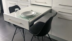 Una cocina moderna con encimera blanca, sillas negras y una mesa de comedor con superficie de vidrio.