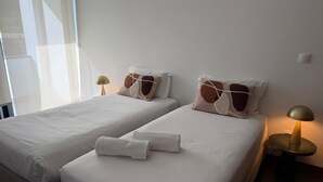 Una habitación de hotel con dos camas, ropa de cama blanca, almohadas marrones estampadas y una mesa redonda con una lámpara.