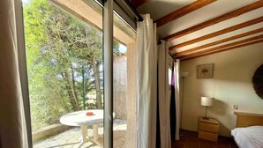 A room with a bed, a nightstand, a table, and a view of the outdoors through a glass door.