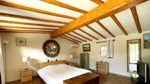 A bedroom with a wooden ceiling, a bed, a dresser, a mirror, and a television.