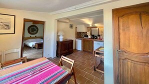 A room with a bed, a dining table with chairs, a kitchen area with a microwave and cabinets, and a wooden door.