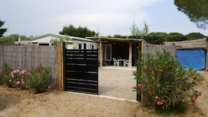 A fenced backyard with a gravel patio, a covered seating area, and flowering plants. - Mobile home in Ramatuelle - plaine de Pampelonne (Ramatuelle)