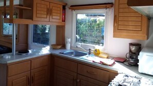 A compact kitchen with wooden cabinets, a sink, and a window overlooking a garden. - Mobile home in Ramatuelle - plaine de Pampelonne (Ramatuelle)