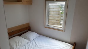 A small, single-bed room with a wooden headboard, a window with a metal grid, and a white wall. - Mobile home in Ramatuelle - plaine de Pampelonne (Ramatuelle)