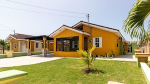 Un edificio giallo con un portico coperto e un piccolo prato con una palma.