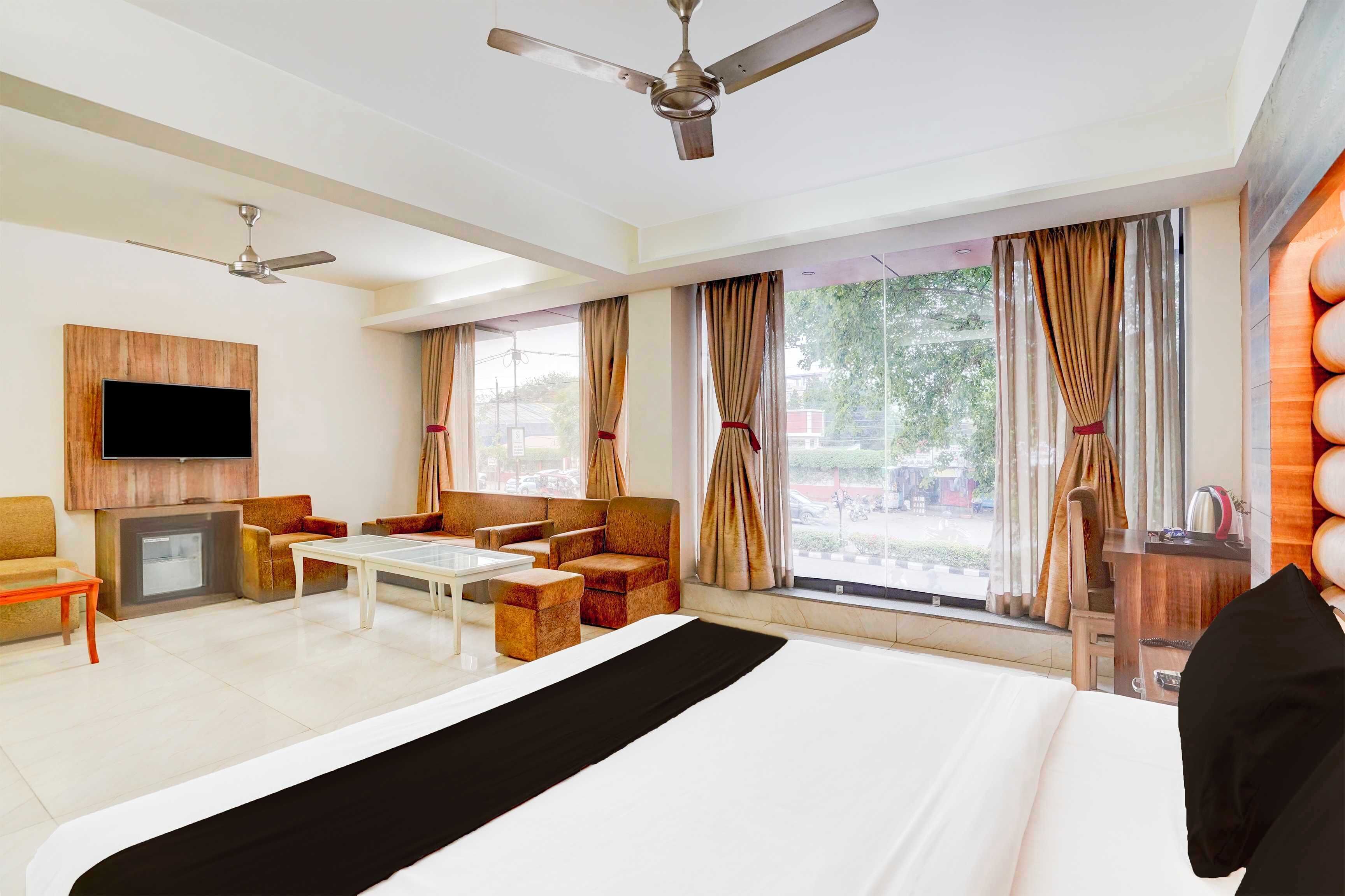 Una habitación de hotel con una cama, televisión, ventilador de techo, chimenea y un ventanal con cortinas.