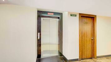 Um elevador, um sinal de saída de incêndio e uma porta de quarto com uma placa.