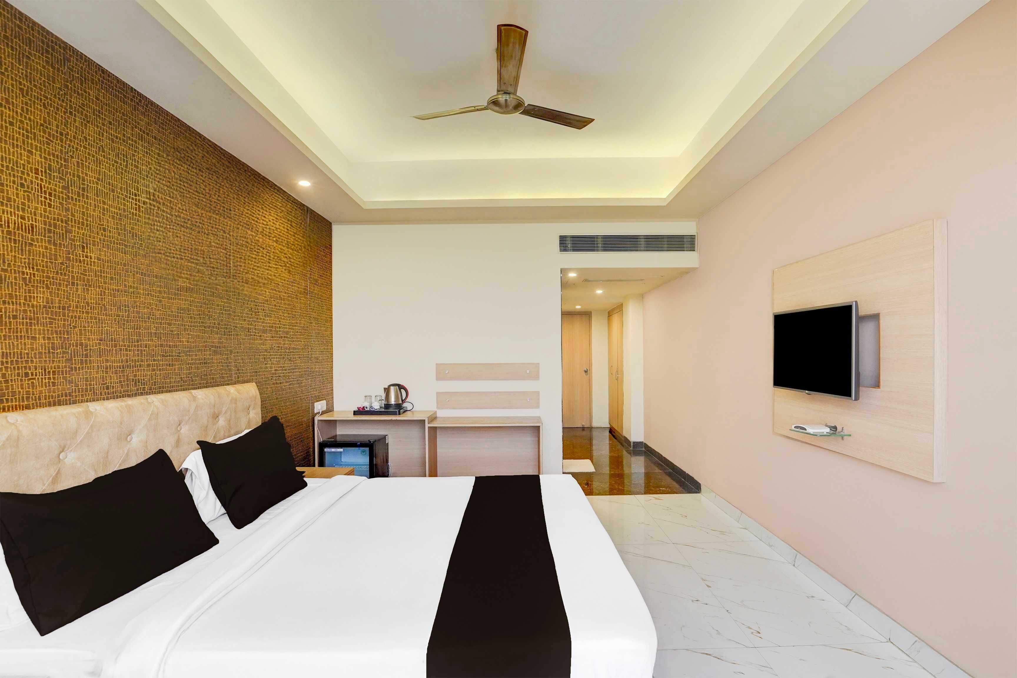 Une chambre d’hôtel équipée d’un lit, d’un ventilateur de plafond, d’une télévision et d’un bureau avec une bouilloire.