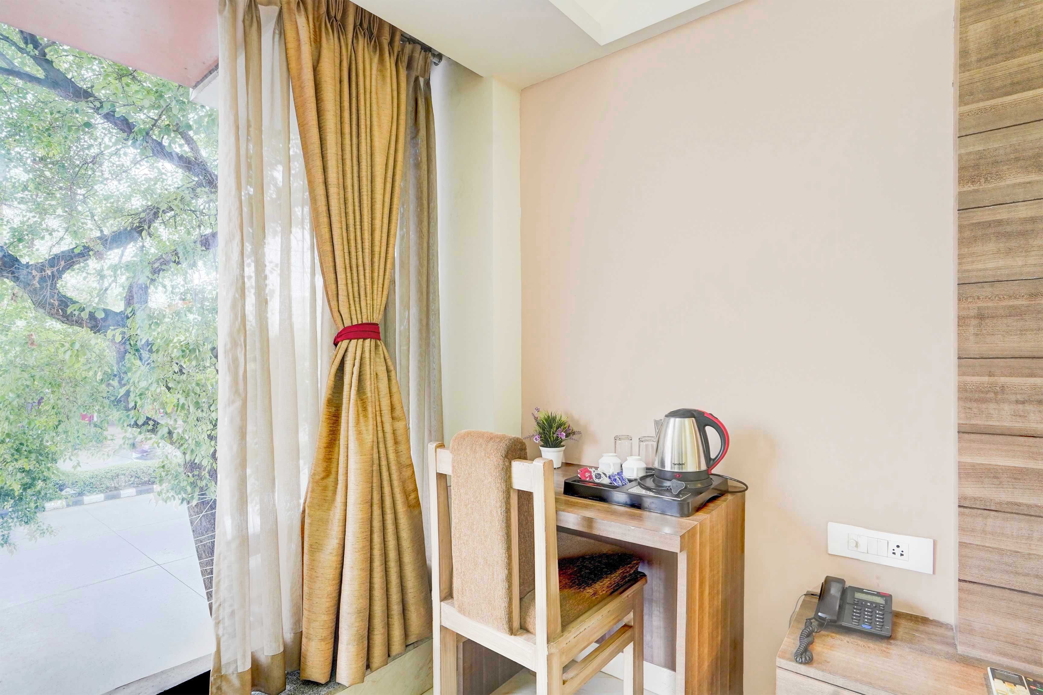 Ein Zimmer mit einem Holztisch, einem Stuhl, einem Telefon, einer Steckdose und einem Fenster mit Vorhängen.