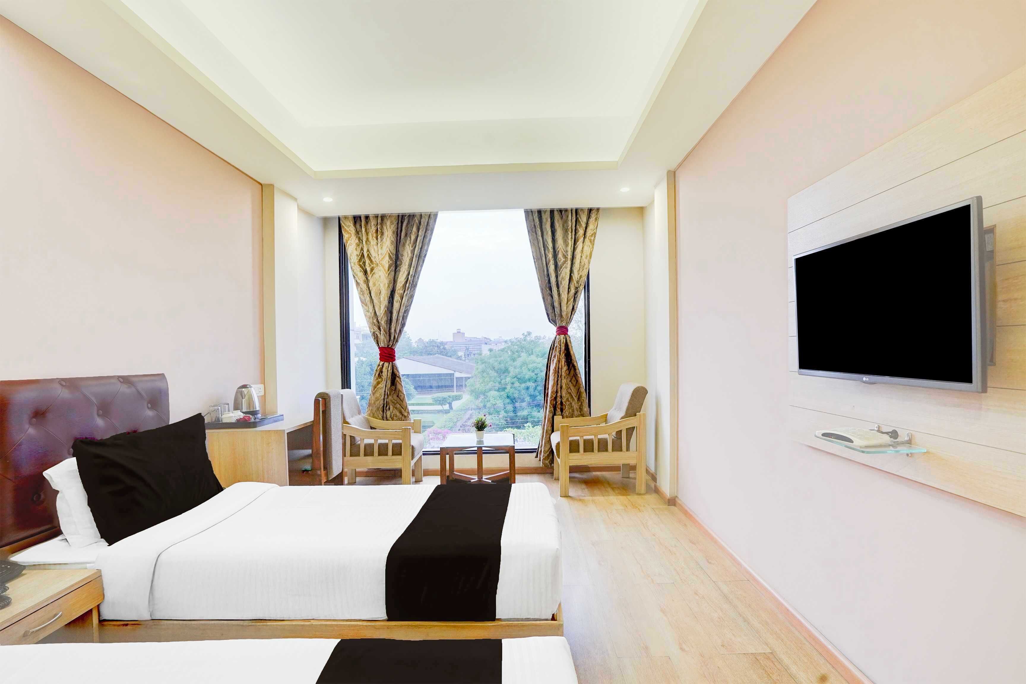 A hotel room with a bed, two chairs, a TV, and a window with curtains.