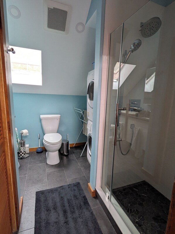 A bathroom with a toilet, washing machine, and glass-enclosed shower area.