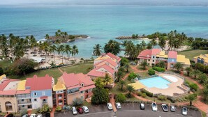 Un resort con varias construcciones, piscina y una playa con palmeras.