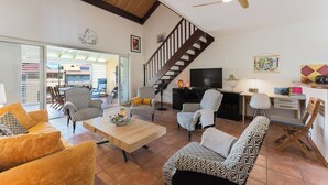 Amplia sala de estar con techo de madera, una escalera, un televisor y un comedor con sillas y una mesa.