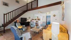 Amplia sala de estar con una escalera de madera, sofás estampados, una mesa de centro y un sillón amarillo.