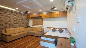 A modern bedroom with a sectional sofa, a bed with a wooden headboard, a ceiling fan, and an air conditioning unit. - Anand's Abode By Yellow Bells (Hyderabad)