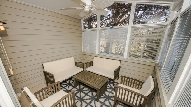 Une terrasse couverte avec un ventilateur de plafond, des sièges blancs rembourrés et un tapis à motifs.