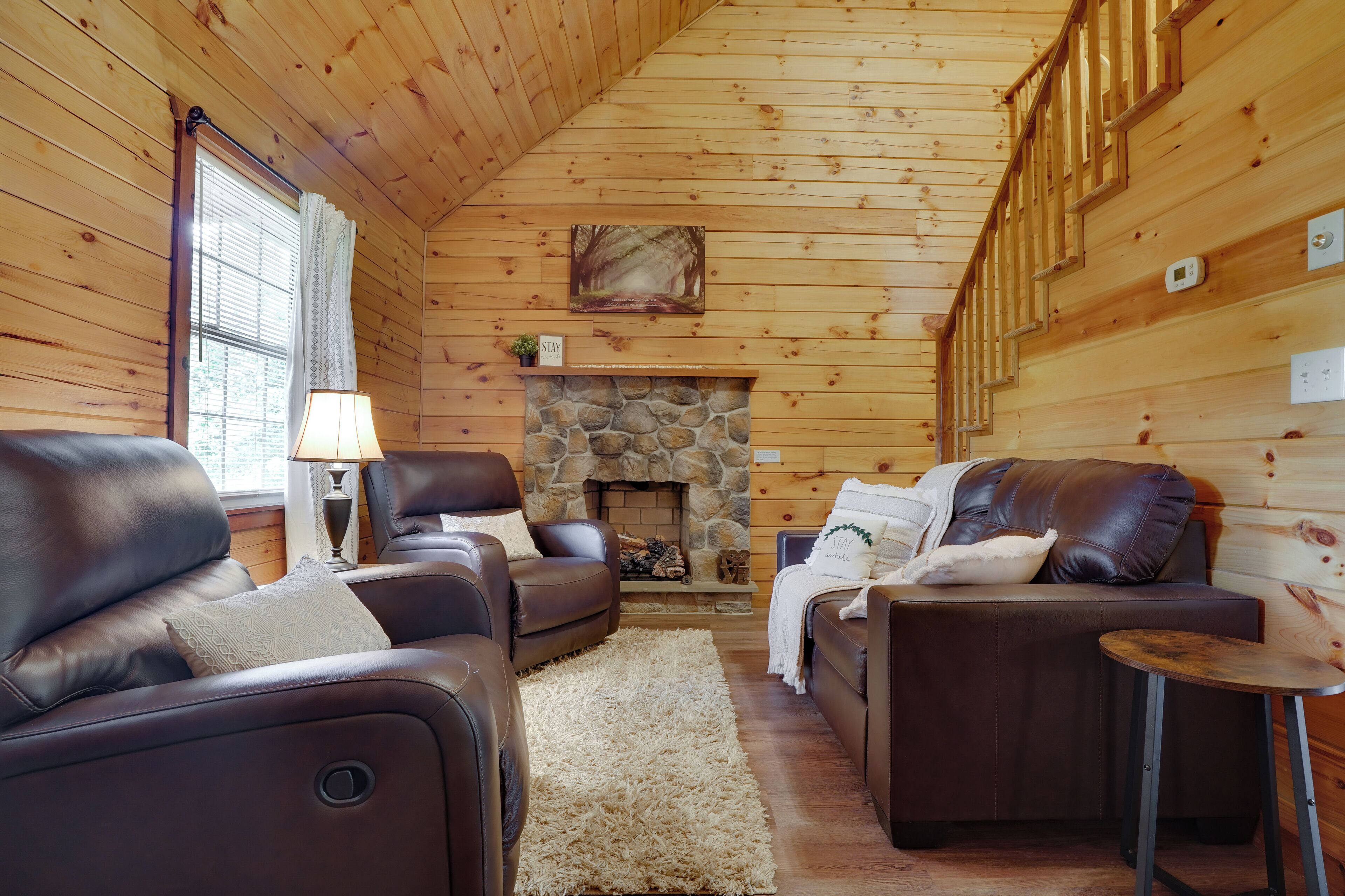 Ein gemütliches Blockhaus-Interieur mit Ledersofas, einem Kamin aus Stein und einer Holzbalkendecke.