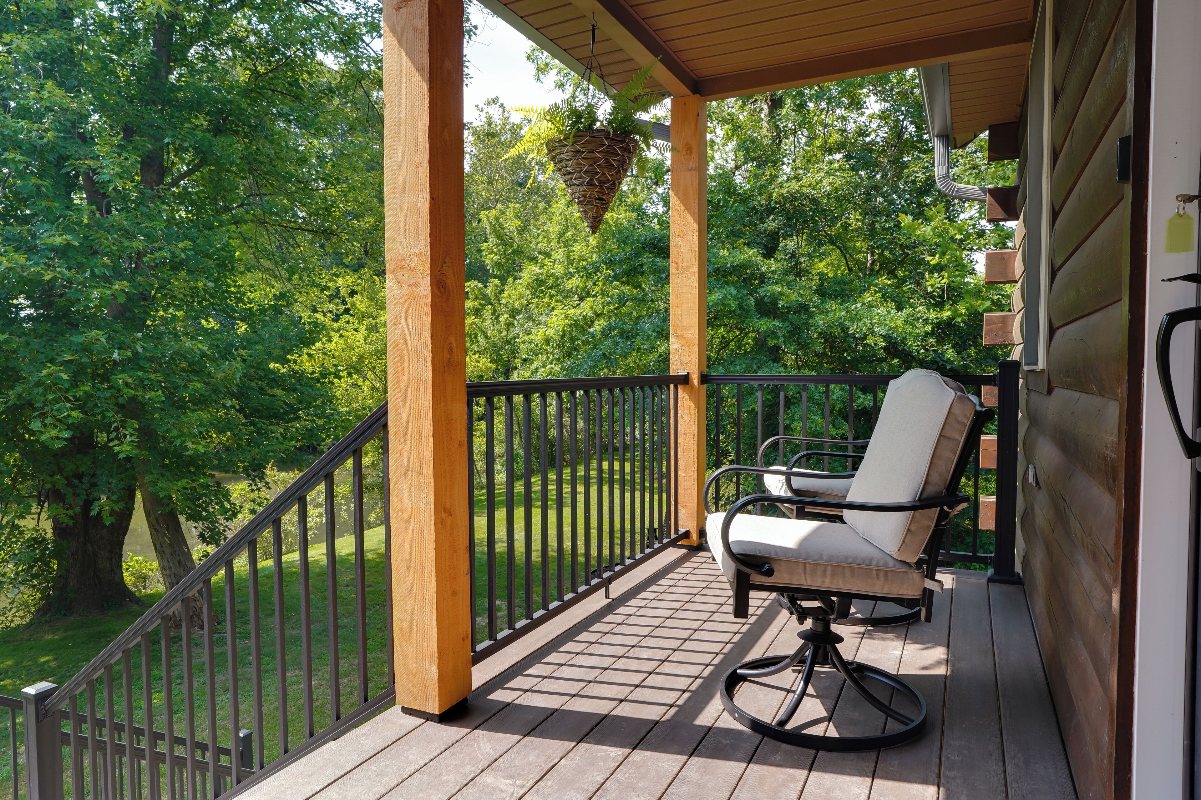 A wooden deck with a black railing, a hanging plant, and a white chair.