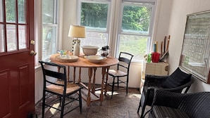 A dining area with a wooden table, four chairs, a lamp, and a view of greenery outside.