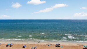 Ein Strand mit blauem Himmel, ruhigem Wasser und Menschen, die schwimmen und sonnenbaden.