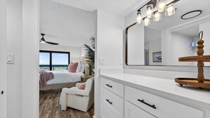 Ein Schlafzimmer mit großem Fenster, einem Bett, einer weißen Kommode und einem Spiegel.