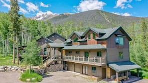 A multi-story lodge with a stone foundation, a covered porch, and a mountain backdrop.