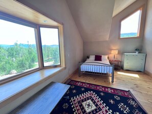 A bedroom with a bed, a nightstand, a dresser, and large windows offering a view of trees and hills. - Aspen Hollow Lodge w/ Hot Tub + Fire Pit (Frisco)