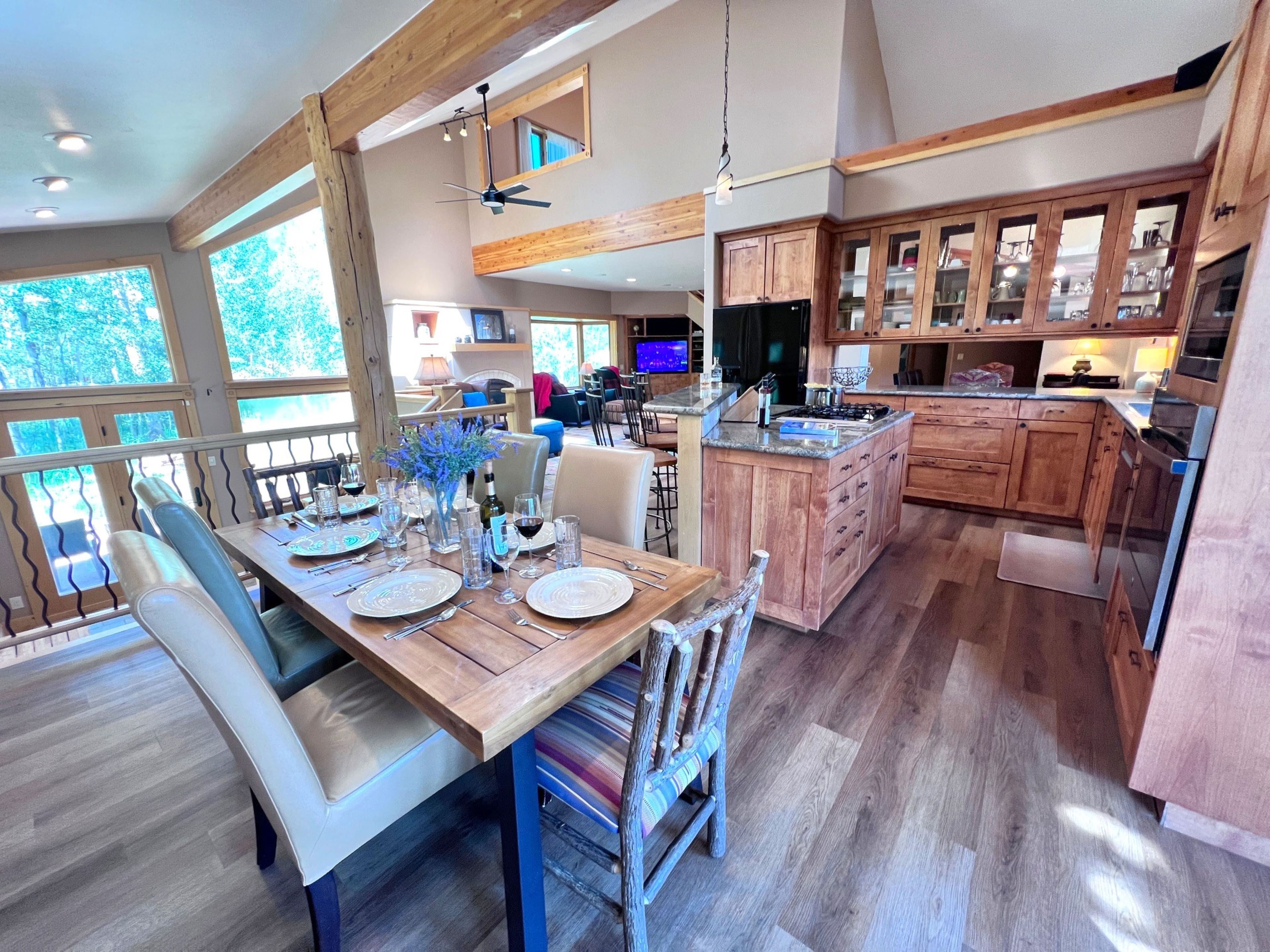 A spacious kitchen with wooden cabinets, a dining area with a wooden table set for six, and a large window overlooking greenery.