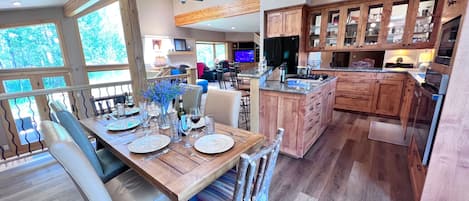 A spacious kitchen with wooden cabinets, a dining area with a wooden table set for six, and a large window overlooking greenery.