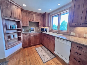 A kitchen with wooden cabinets, a dishwasher, a microwave, and a window providing natural light.