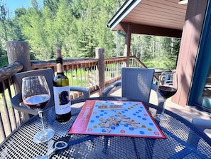 A Scrabble game on a metal table outdoors with a bottle of wine and glasses.