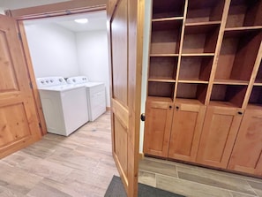 A laundry room with two washing machines and a wooden shelving unit.