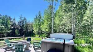 An outdoor hot tub area with a wooden deck, green Adirondack chairs, and a stone fire pit.