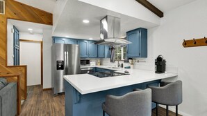 A modern kitchen with blue cabinets, a stainless steel refrigerator, a built-in oven, and a large island with bar stools.