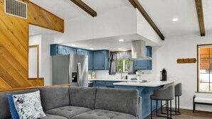 A modern kitchen with blue cabinets, a stainless steel refrigerator, and a central island with bar stools.