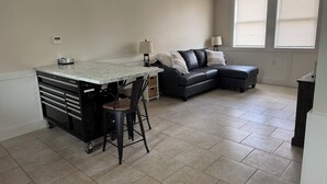 A modern kitchen with a marble countertop, a black leather sofa, and a dining area.