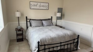 A neatly made bed with a patterned bedspread, two bedside lamps, a small bedside table with a lamp, and a wall-mounted sign that reads "sweet dreams".