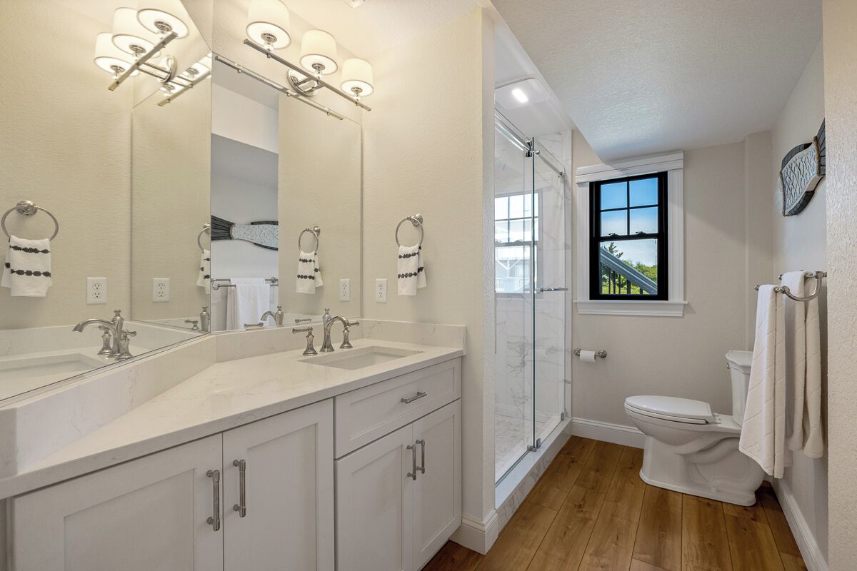 A bathroom with two sinks, a large mirror, a toilet, and a shower.