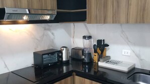 Una cocina moderna con armarios de madera, encimera negra, horno integrado, cafetera, tostadora, licuadora y bloque para cuchillos.