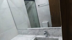 Un baño con lavabo de mármol, cabina de ducha con paredes de vidrio y un inodoro.