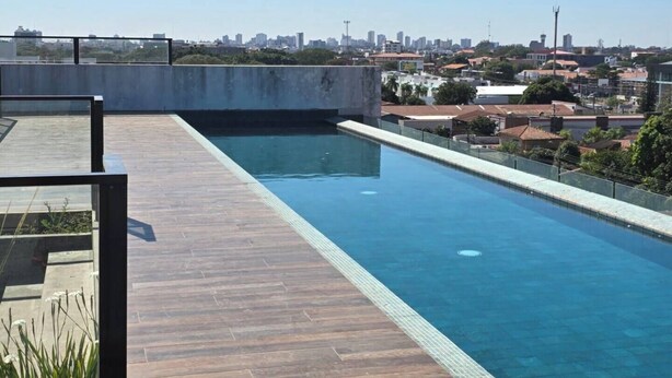 Una piscina en la azotea con terraza de madera y vistas a la ciudad.