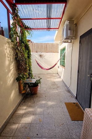 A narrow outdoor corridor with a hammock, potted plants, a tiled floor, and a door on the right.