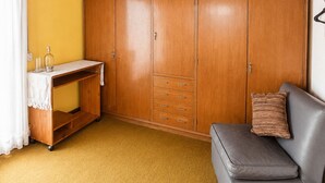 Une pièce avec une armoire en bois, une petite table recouverte d’une nappe blanche, un canapé gris et un mur jaune.