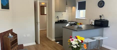 Una cocina moderna con una isla central, taburetes de bar y un comedor con mesa y sillas de madera.