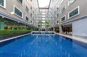 A swimming pool with a tiled floor, surrounded by a multi-story building with large windows and a flat roof. - Sunday Grand Jomtien Pattaya (Pattaya)