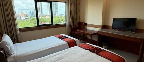 A hotel room with two beds, a desk, a television, and a window with a city view.