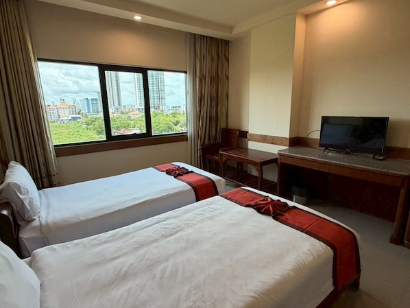 Habitación de hotel con dos camas, un escritorio, televisor y ventana con vistas a la ciudad.